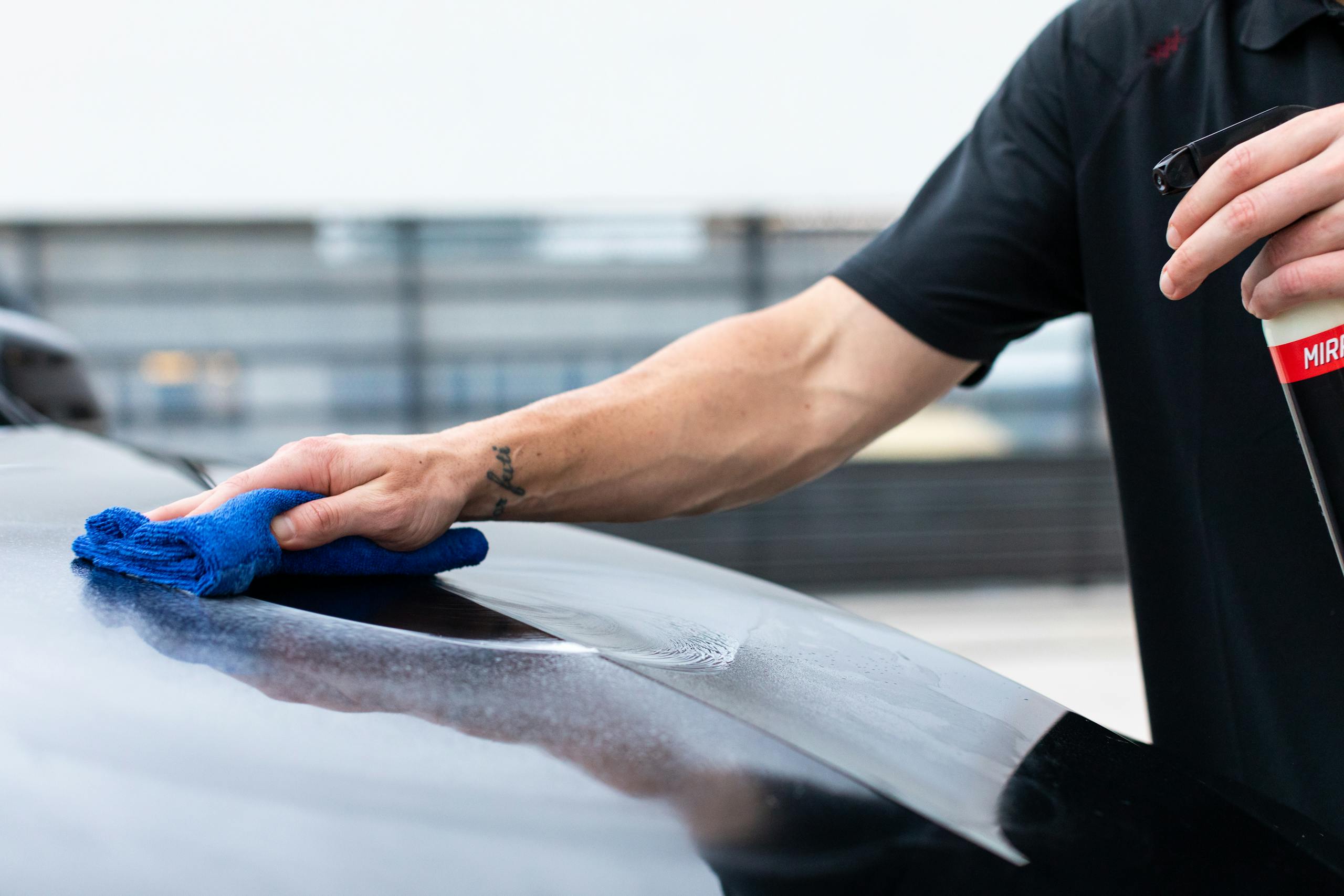 Close-up of hand cleaning car with cloth and spray bottle for maintenance.