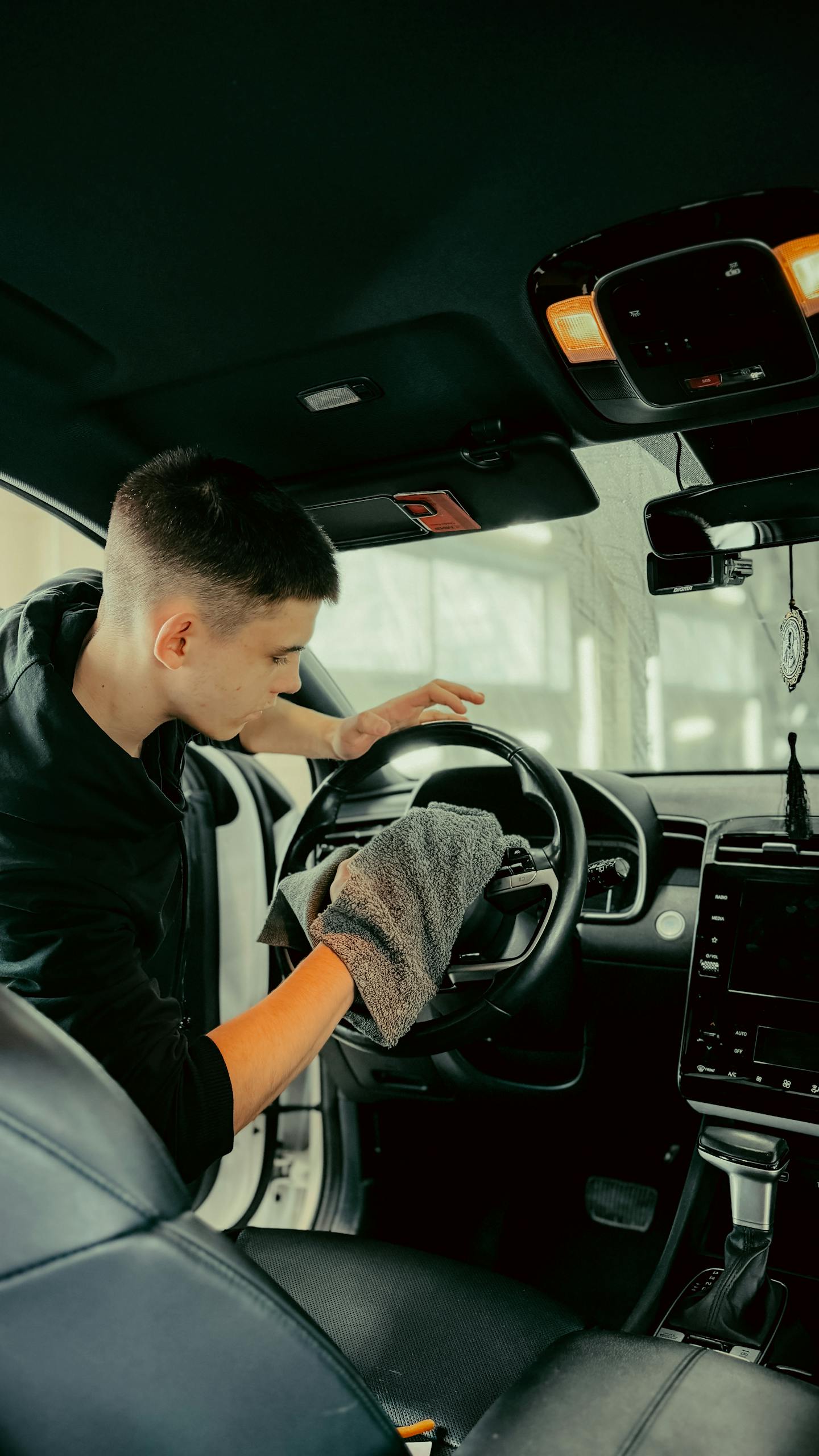 Young man polishing car steering wheel with cloth, ensuring clean interior.